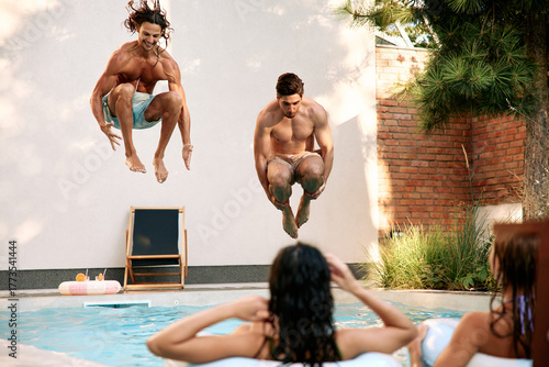 Men jumping into swimming pool while friends watch and enjoy summer vacation