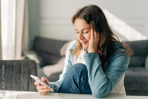 Brunette woman at home looking at her smartphone on a sofa in natural light today