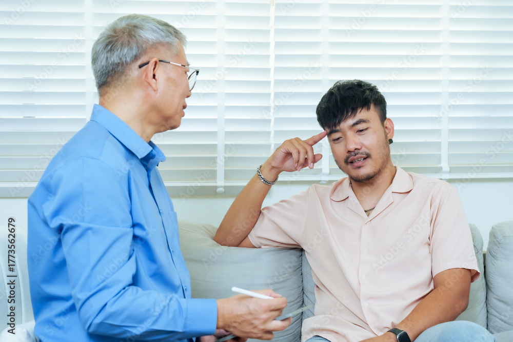 Obraz premium Asian adult man pointing to head during counseling with senior psychiatrist, discussing emotional challenges and receiving professional guidance for stress management and psychological healing