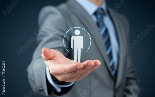 Professional photo of a businessman in a light gray suit and blue tie holding a glowing white holographic butterfly above his palm. The wireframe butterfly has blue outlines and a human figure design.