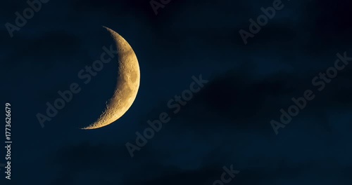 Waxing crescent moon slowly sinking behind dark clouds at night. Timelapse of the moon disappearing into the horizon, atmospheric night sky with dramatic shadows.