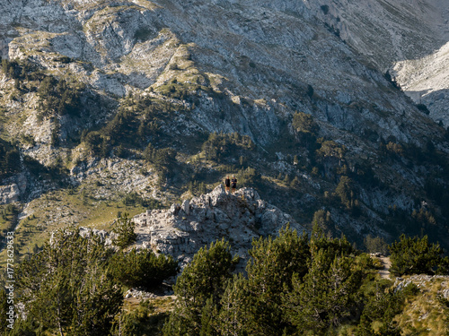 Wallpaper Mural Aerial view of a rugged, mountainous landscape with scattered trees and rocky outcrops, where two figures stand silhouetted against the sky, Teth, Shkoder County, Albania. Torontodigital.ca