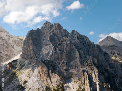 Aerial view of jagged, grey mountain peaks jut towards the azure sky, a rugged landscape etched in stone, Teth, Shkoder County, Albania.