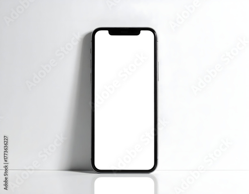 A black smartphone stands vertically against a white wall, featuring a blank white screen ready for content.