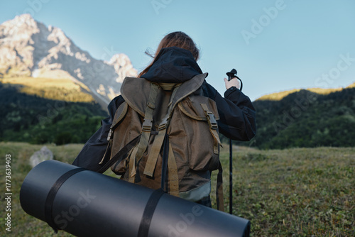 A lone adventurer wearing a sturdy backpack marches across a wide meadow toward looming mountains under a clear sky, preparing for a hike and outdoor exploration.