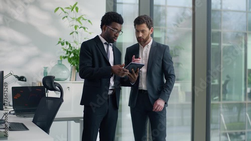 Two multiracial businessmen discussing project in modern office looking at digital tablet together multiethnic business men diverse male colleagues talking cooperation teamwork strategy planning work