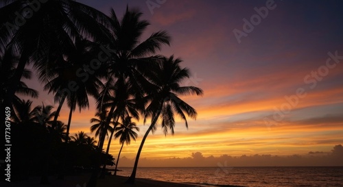 Silhouetted palms against vibrant sunset sky with beach and ocean in foreground