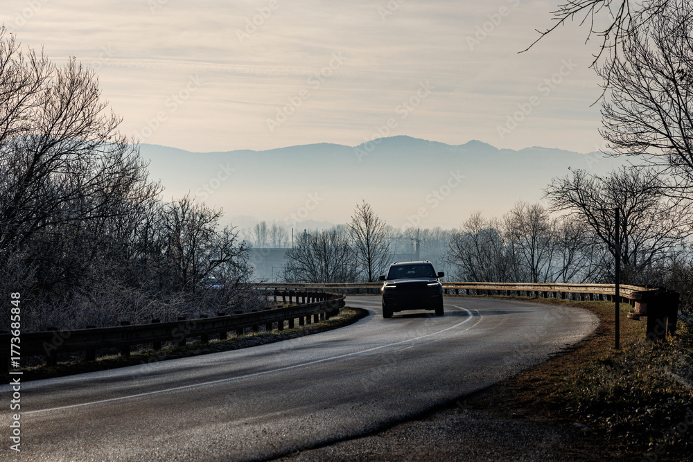 Fototapeta premium Car driving on curved winter road in misty mountains