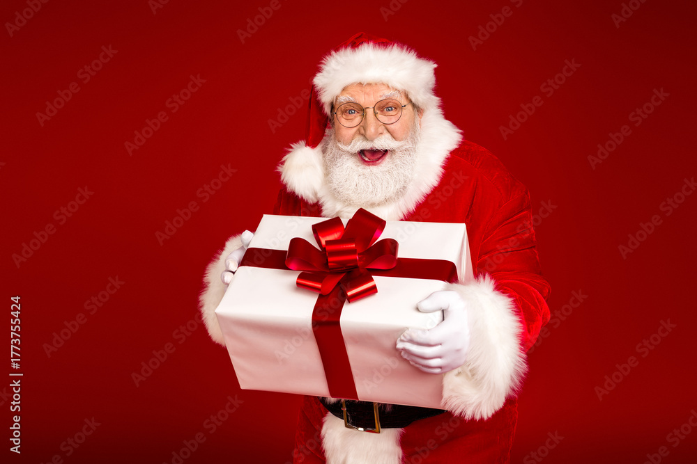 Naklejka premium Santa Claus delivers a festive Christmas gift box full of joy to a bright red background capturing holiday magic warmth and family celebration