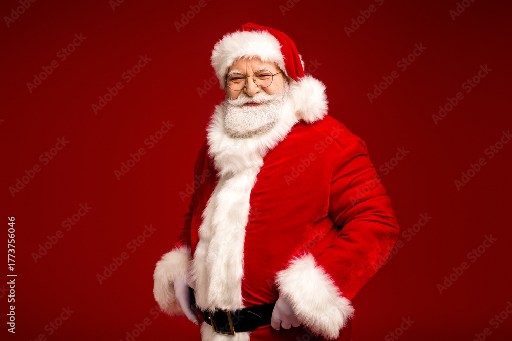 Naklejka premium Santa Claus in red suit with white fur trim smiles confidently against a rich red background ready for holiday celebration and seasonal shopping