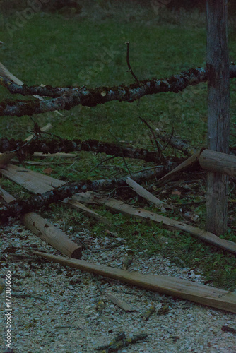 A wooden split-rail fence with broken and moss-covered sections borders a gravel path next to a grassy area and dark trees in the evening