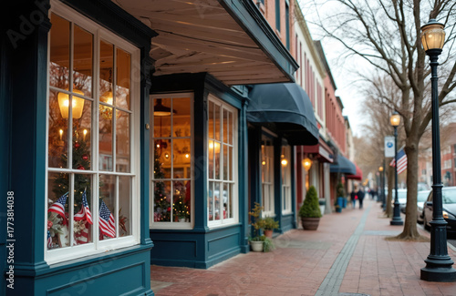 Fototapeta Naklejka Na Ścianę i Meble -  Small town main street shopfront view decorated for Christmas holiday season. American flags visible on display. Quaint stores with light on windows. Classic street view with architecture and lights.