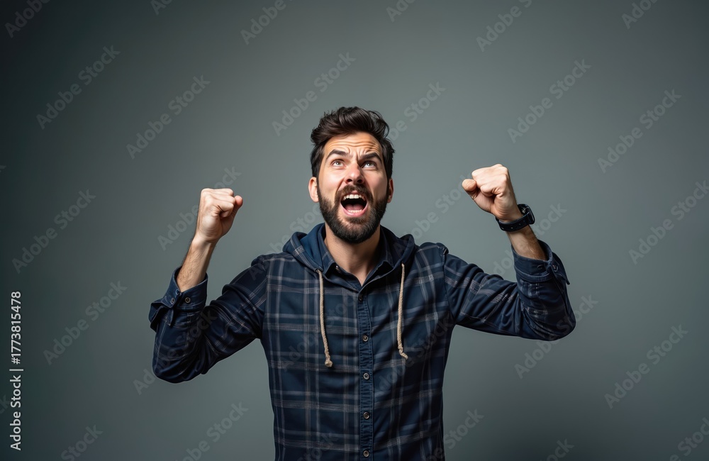 Fototapeta premium Man with beard shouts loudly raising fists in air. Intense male feels frustration anger or extreme emotion. He gesticulates wildly, showing facial expression of rage.