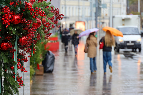 New Year decorations in city, red Christmas balls on a street on blurred background of people with umbrellas during rain