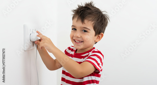Young child inserts electrical plug into a wall outlet smiling indoors