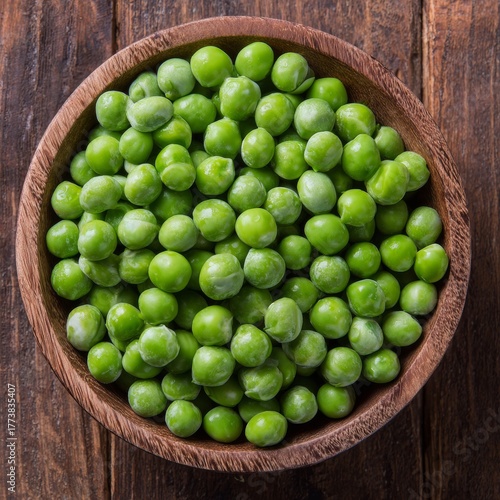 A bowl of fresh green peas. The peas are sitting inside of a wooden bowl on a wooden table. 