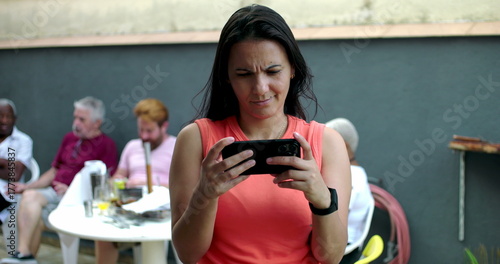 Tableau sur toile Woman frowning at smartphone screen, confused and frustrated, standing outdoors,