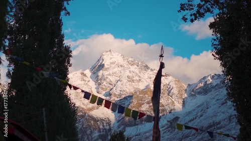 Slow motion shot of defocused prayer flags waving in front of snowy Himalayan mountain peak during the sunset as seen from Keylong in Lahaul and Spiti district, Himachal Pradesh, India. Scenic view. 