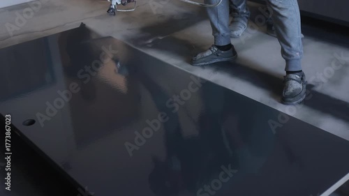 Painter applies smooth coat of navy paint to large tabletop, revealing fresh look in renovated room.