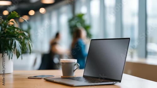 Wallpaper Mural A minimalist office setup features a closed laptop, coffee cup, and smartphone on a wooden desk, surrounded by plants and large windows. The scene exudes calm, focus, and modern productivity Torontodigital.ca