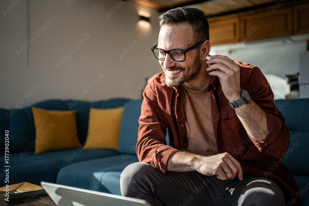 Obraz premium Man having video call with wireless earbuds working from home