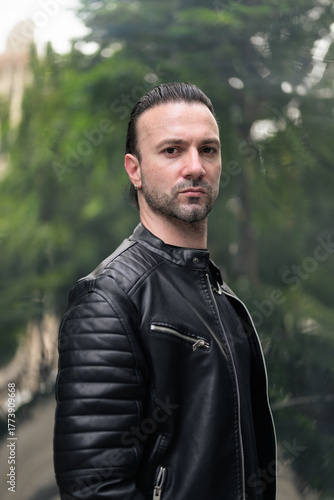 Handsome bearded man in black leather jacket posing in city