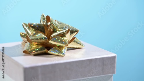 Gift box with golden bow turns on blue background.