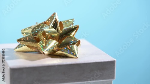 Gift box with golden bow turns and blurs on blue background.