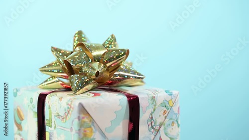 Christmas gift box with golden bow turns on blue background.