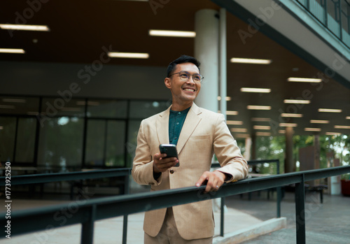 Smiling Asian businessman holding phone standing in modern building