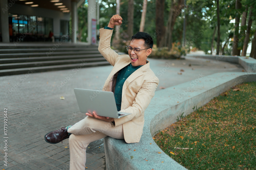 Fototapeta premium Businessman celebrating success receiving good news on laptop outdoors