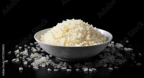 A bowl of fluffy white cooked grains, spilled grains on a glossy black surface