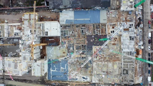 Direct overhead drone shot of large-scale residential building construction site with visible cranes, frameworks, and workers. Urban housing and industry progress.