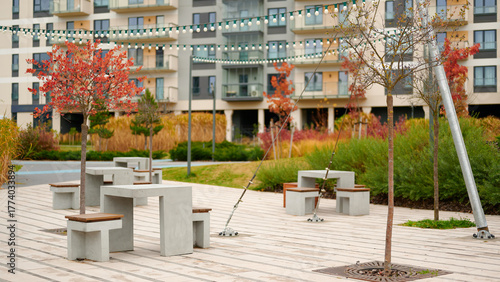 modern urban courtyard scene features concrete benches and autumn trees near apartment buildings. inviting outdoor space ideal for relaxation and community gatherings, with string lights creating