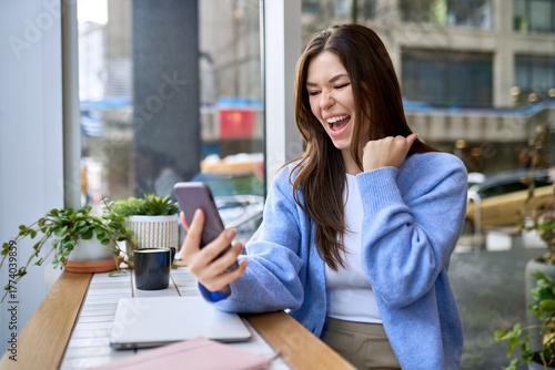 Happy young woman student feeling excited winner holding cellphone using mobile phone winning online, receiving great news or sms offer looking at smartphone, getting new job celebrating success.