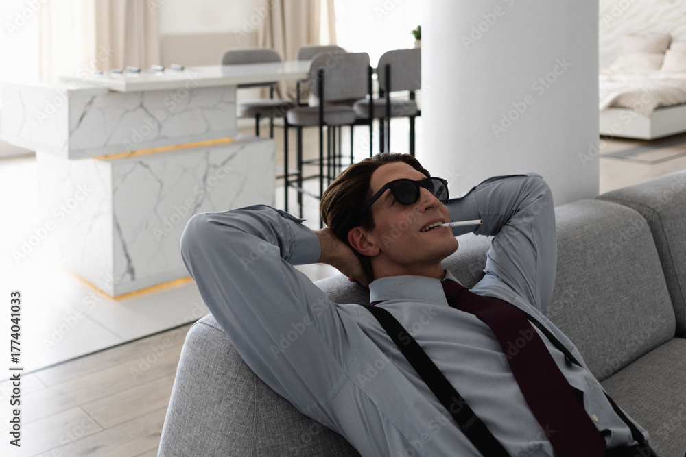 Fototapeta premium A successful and confident young yuppie smokes in his perfect apartment while sitting on the couch