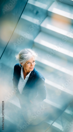 Senior businesswoman at modern office. Top view portrait of older woman in office stairwell. Vertical blurred bright background. Concept image of business.