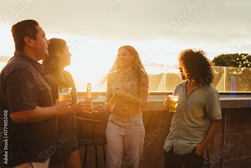 Group of young friends drinking beer and talking at a rooftop bar during sunset