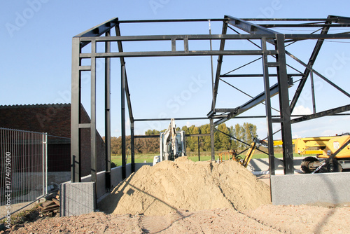 the steel construction of a shed and a heap of sand and excavators during the building of a shed in the countryside