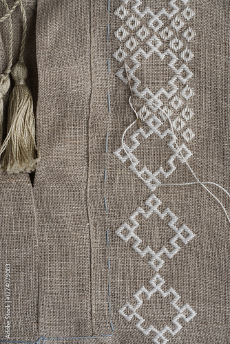close-up of a beige linen shirt, hands embroidering traditional Ukrainian embroidery. The process of working on embroidery, handwork in traditional technique
