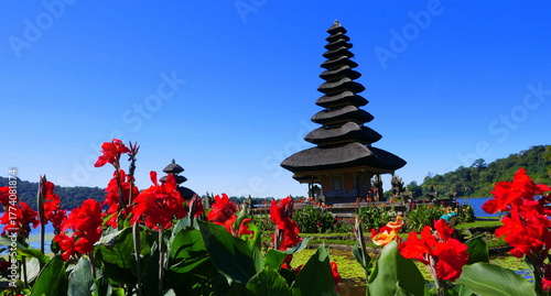 Hoher Turm des Bratantempels mit roten Blumen im Vordergrund unter blauem Himmel 