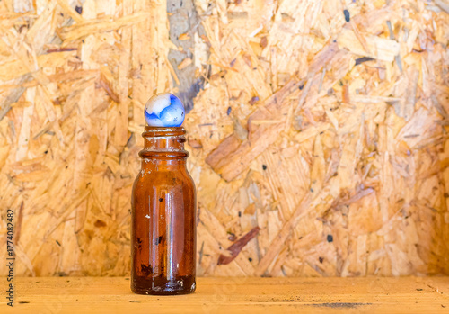 Closeup of Antique Amber Colored Bottle Topped with a Vintage Marble and a Particle Board Wood Background