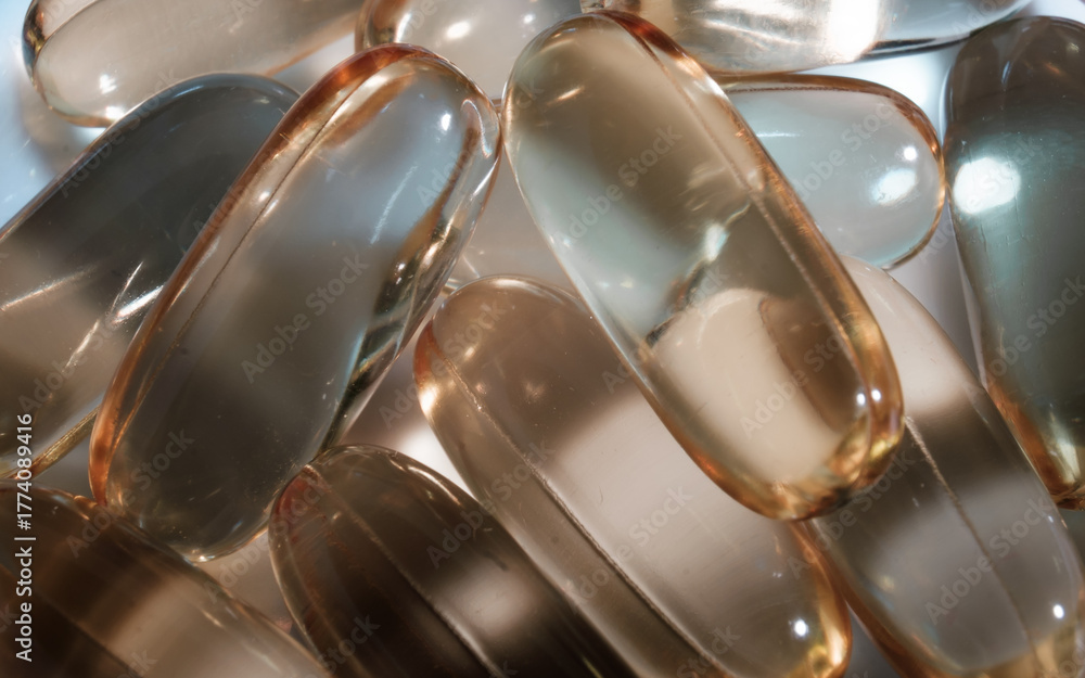 Naklejka premium Zbliżenie na stos owalnych, przezroczystych kapsułek z suplementami diety, o bursztynowej barwie. Kapsułki są ułożone losowo, a ich lśniąca powierzchnia odbija światło.
