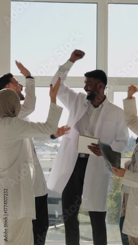 Vertical video. Multicultural medical team celebrating a victory with high fives, smiling doctors and nurses united in a bright modern clinic