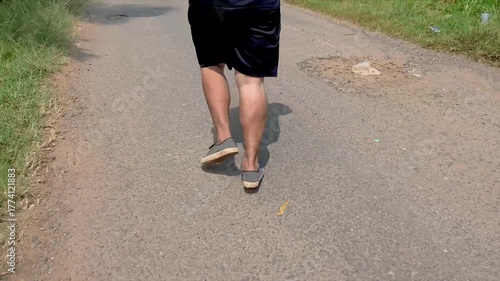 Close up of a man in black sports uniform and black sneakers running along an asphalt road in the countryside