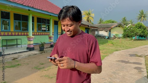 Man using smartphone outdoors near colorful building in rural setting