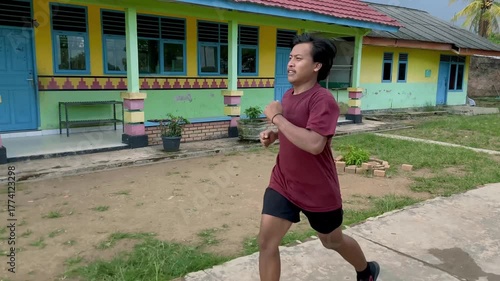A young Asian man wearing sneakers runs on an asphalt road in slow motion. A portrait of some men exercising in the afternoon. Fitness concept.