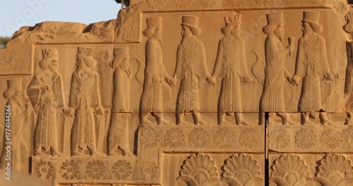 Warm raking light reveals a Persepolis relief of Persian dignitaries in procession—carved robes, curled beards, lotus and rosette borders. Achaemenid ceremony and craftsmanship preserved in stone.