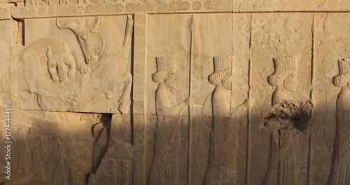 Wallpaper Mural Wide relief panel at Persepolis shows iconic lion attacking bull beside a procession of Persian dignitaries and rosette borders. Warm raking light reveals texture, ceremony, mythology, imperial power. Torontodigital.ca