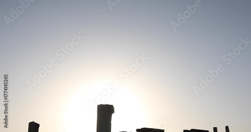 Backlit view of Persepolis as the sun drops behind the plateau: broken columns, doorways and porticos in dark silhouette. A quiet desert dusk evoking endurance, empire, and timeless memory of stone.